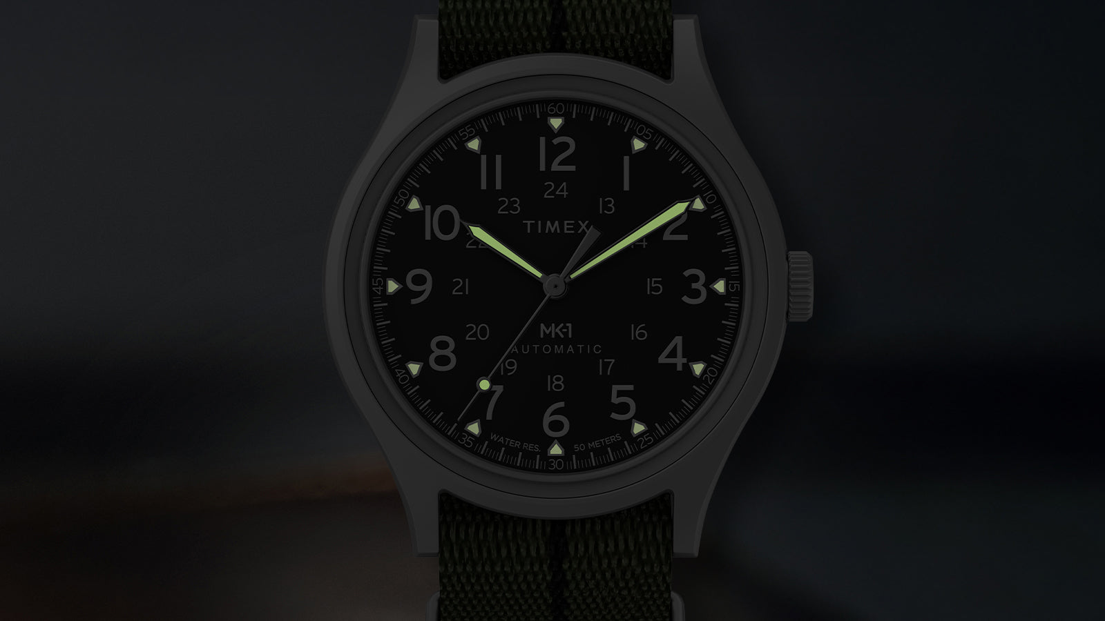 Timex MK1 Automatic dial in low light highlighting luminous hands and hour markers.