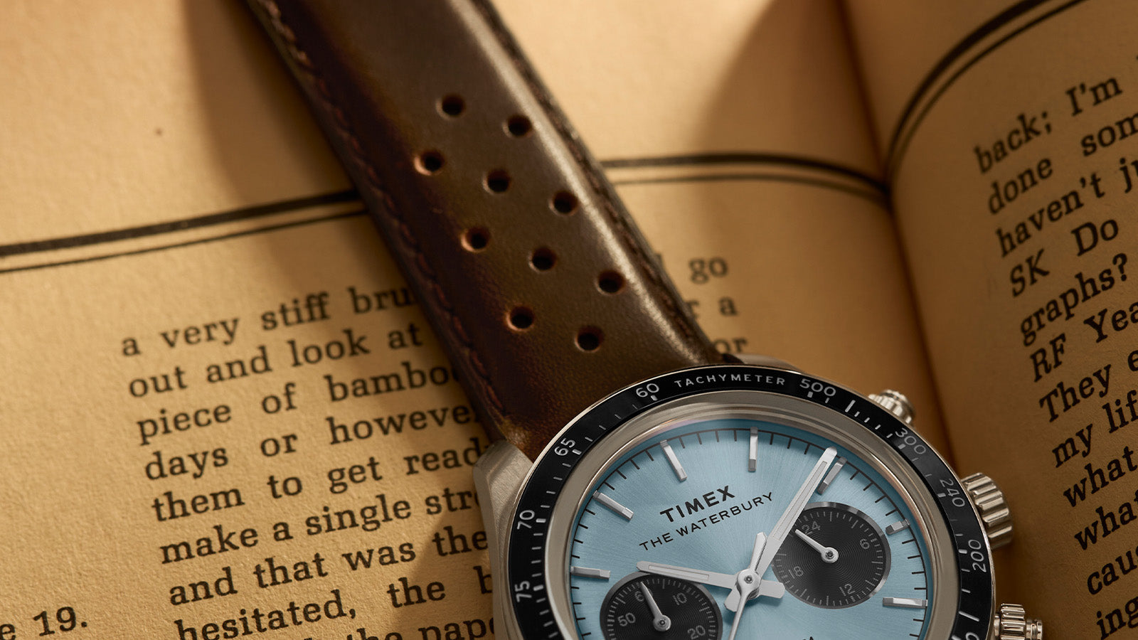 Timex Waterbury Heritage Chronograph with brown leather strap and light blue dial, resting on an open vintage book.