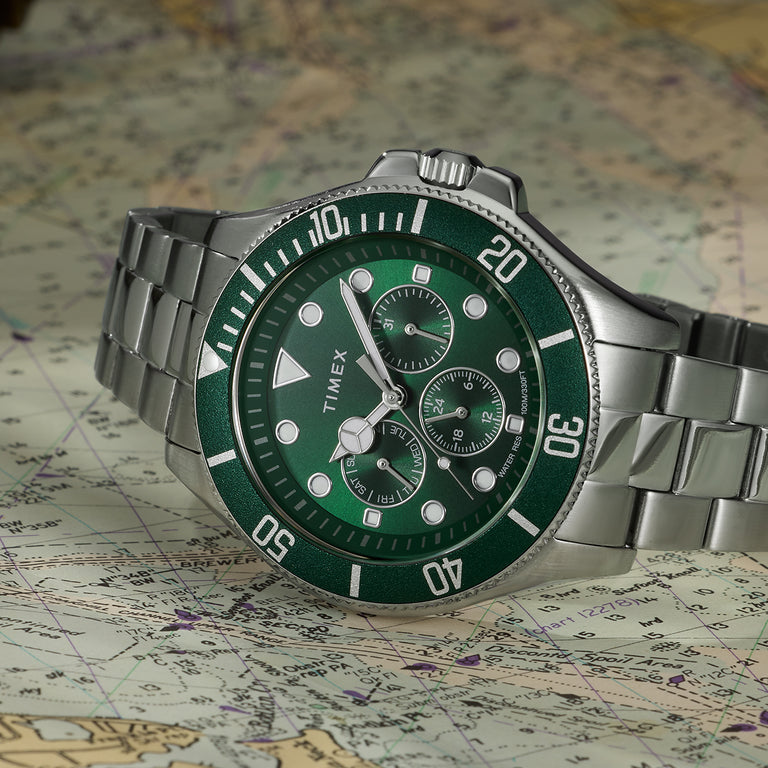 Timex Harborside watch with green dial and bezel, stainless steel bracelet, and chronograph subdials displayed on nautical map background.