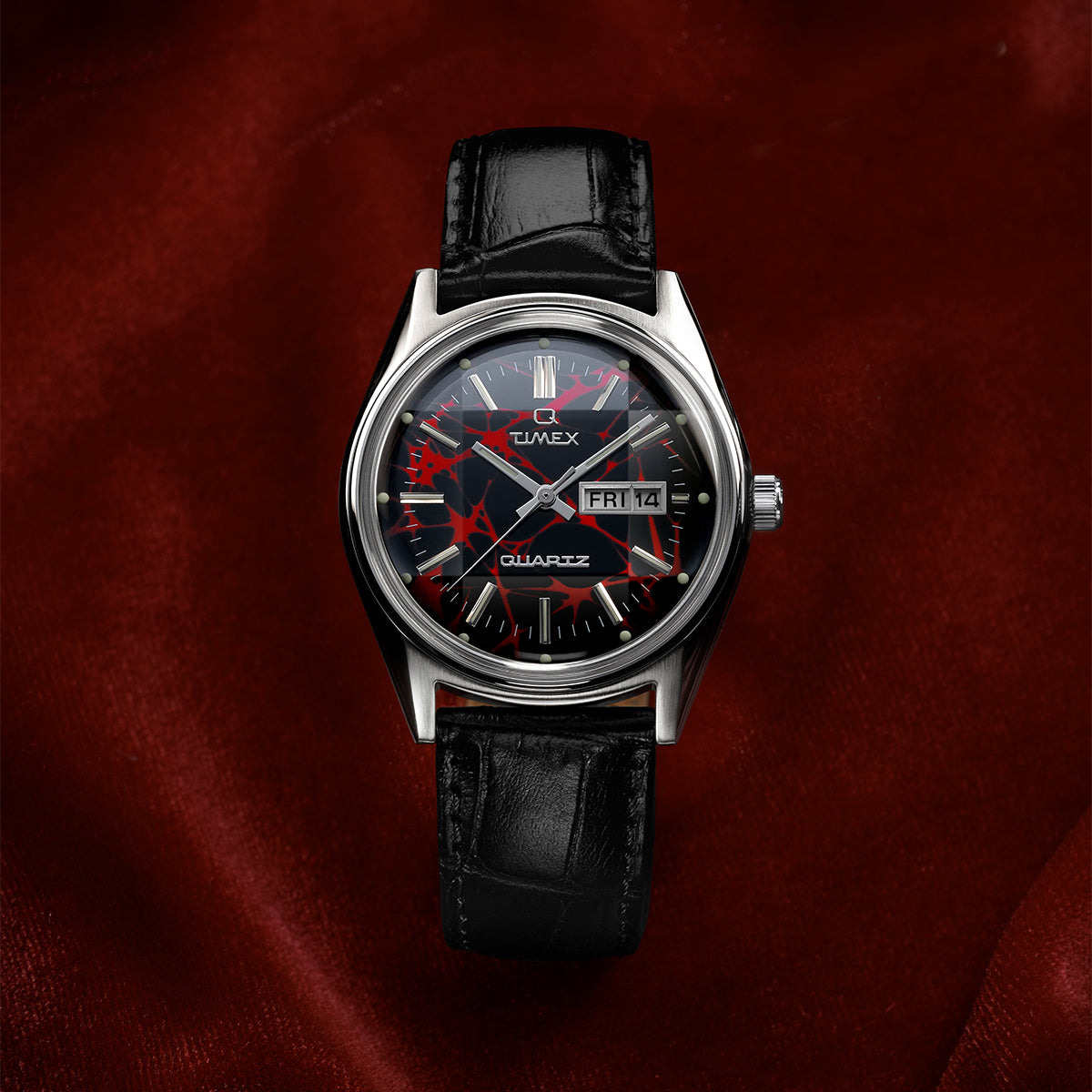 Front view of the Q Timex® Red Vega 1978 Reissue watch showing the red and black patterned dial, day-date window, and black leather strap.
