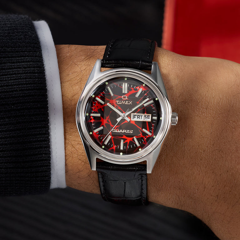 Q Timex® Red Vega 1978 Reissue watch worn on the wrist, highlighting the red patterned dial, day-date display, and black leather strap.