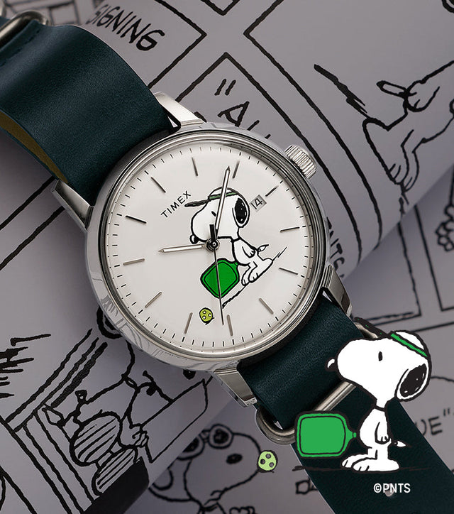 Peanuts® x Timex Marlin® Automatic Pickleball watch with Snoopy pickleball dial and green leather strap displayed on Peanuts comic strip background.
