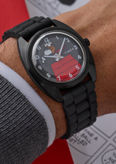 Peanuts® x Timex 1979 Reissue Inspired watch worn on wrist, featuring a black case and bracelet with Snoopy as the Flying Ace on a gray dial above his red doghouse.