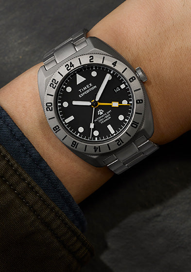 Expedition® Pioneer Titanium Automatic GMT watch worn on the wrist, featuring a titanium case and bracelet, black dial, 24-hour bezel, and yellow GMT hand.