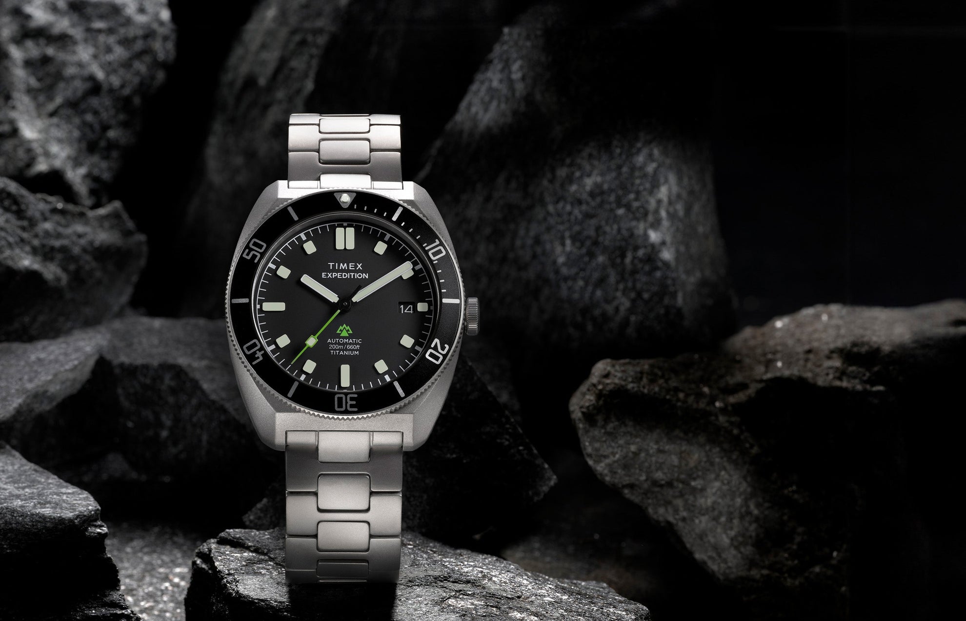 Expedition® Pioneer Titanium Automatic standing on rugged rocks, highlighting the titanium bracelet, black dial, rotating bezel, and date window.