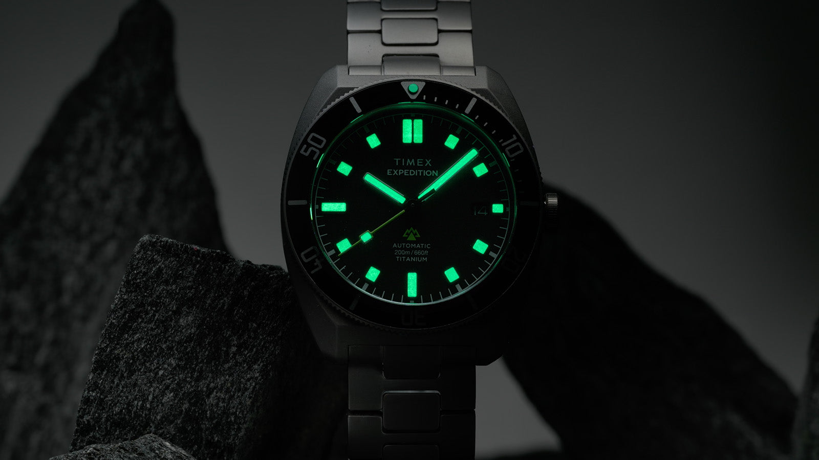 Low-light image of the Expedition® Pioneer Titanium Automatic with fully illuminated hands and hour markers glowing green in the dark.