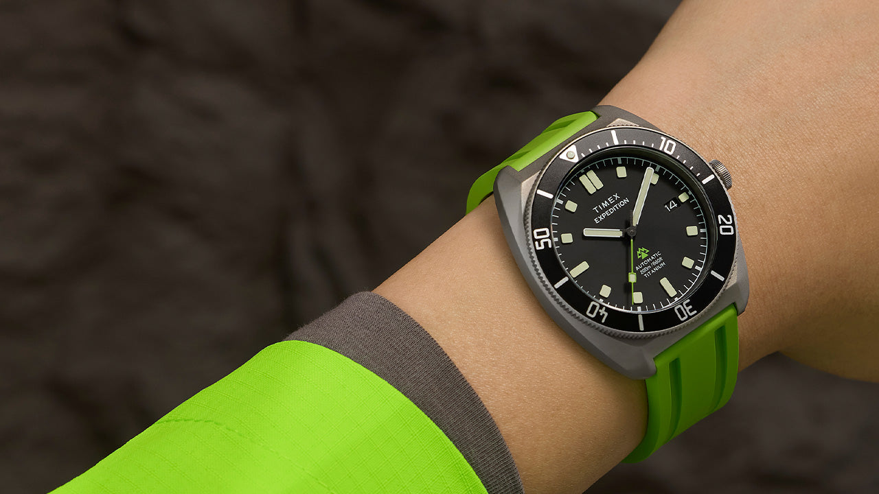Expedition® Pioneer Titanium Automatic watch worn on the wrist, featuring a matte titanium case, black dial, and bright green rubber strap.