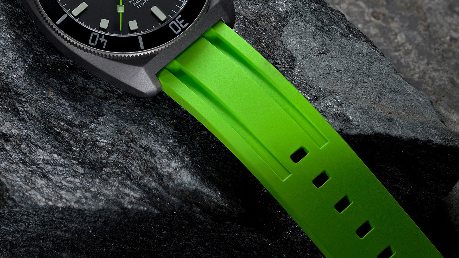 Close-up of the textured green rubber strap and titanium case resting on stone.