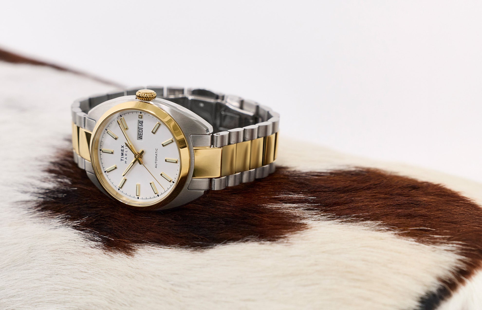 Timex Marlin® Draper Automatic two-tone stainless steel watch resting on a textured surface, featuring a white dial and gold-tone accents.