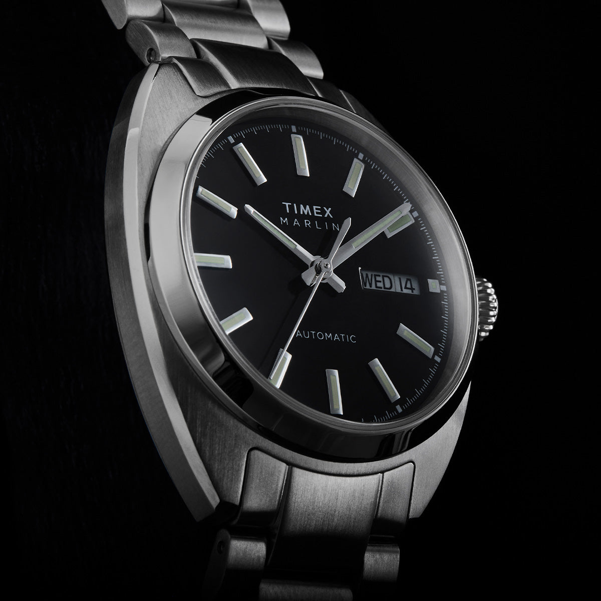 Close-up of the Timex Marlin Draper Automatic black dial with luminous hour markers, silver hands, and day-date display.