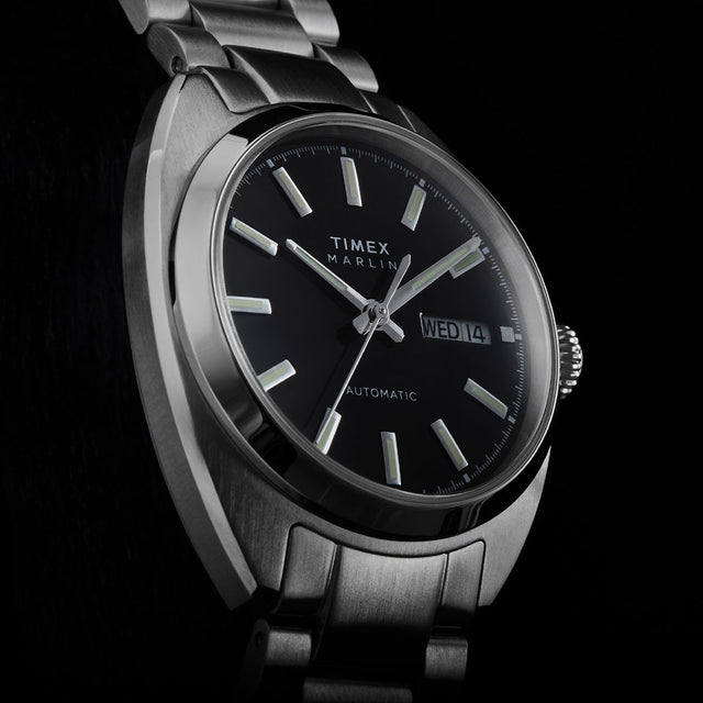Close-up of the Timex Marlin Draper Automatic black dial with luminous hour markers, silver hands, and day-date display.