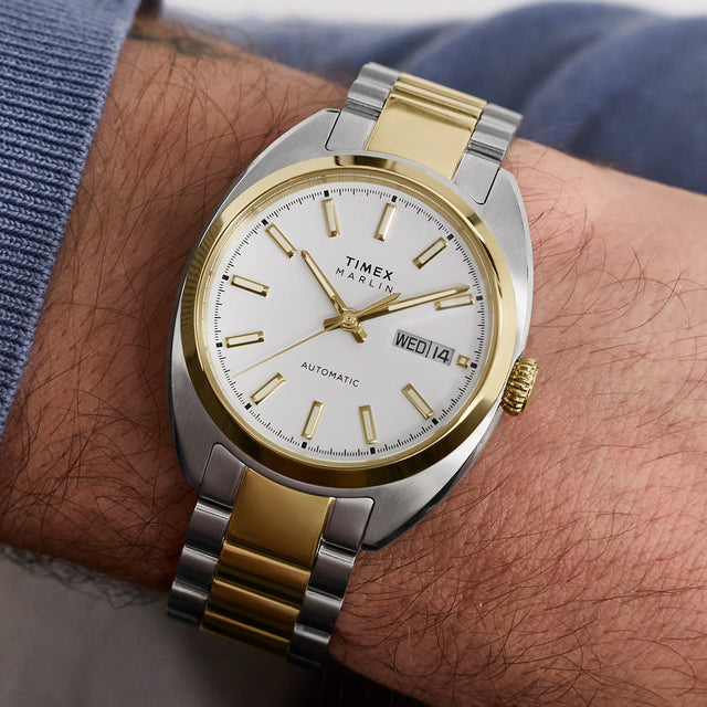 Timex Marlin® Draper Automatic two-tone watch worn on the wrist, showing a white dial, day-date window, and stainless steel and gold-tone bracelet.