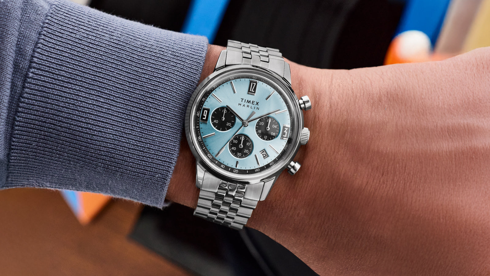 Timex Marlin Chronograph Tachymeter watch with a light blue dial and stainless steel bracelet worn on a wrist, featuring black chronograph subdials and a tachymeter scale.