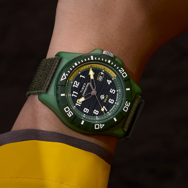Angled wrist shot of Timex Expedition® Freedive Solar watch featuring green case, black textured dial, yellow second hand, and black fabric strap.
