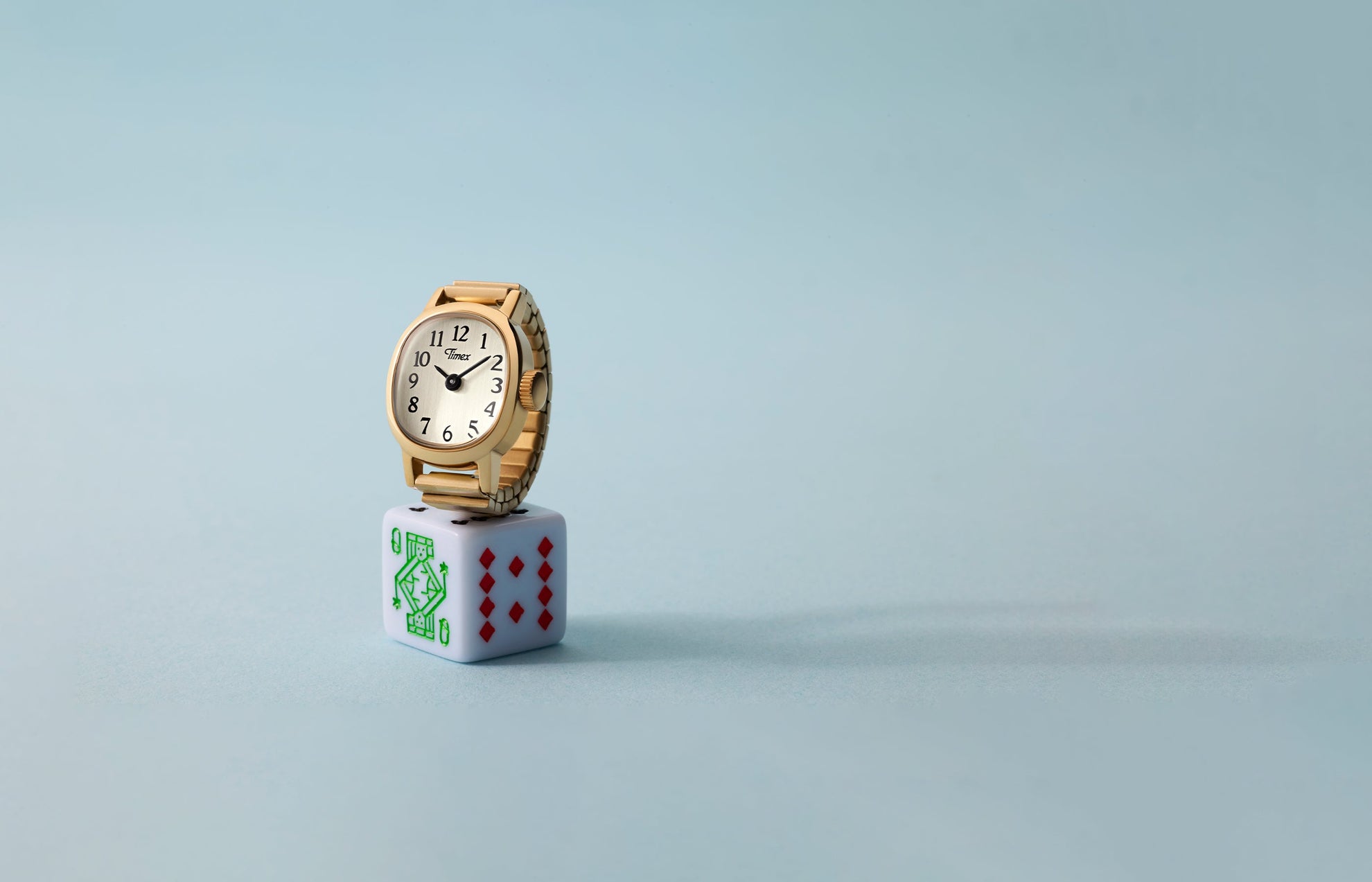 Timex Cavatina® Mini gold-tone watch with champagne dial displayed on white playing die against soft blue background.