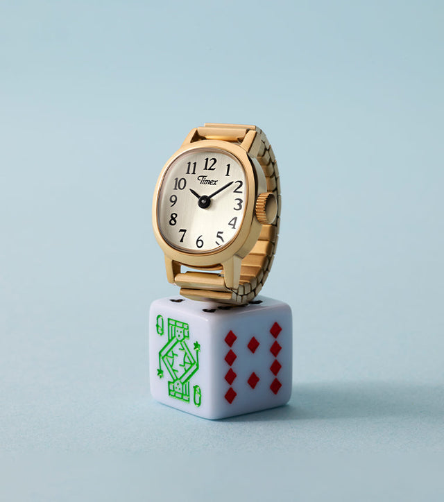 Timex Cavatina® Mini gold-tone watch with champagne dial displayed on white playing die against soft blue background.