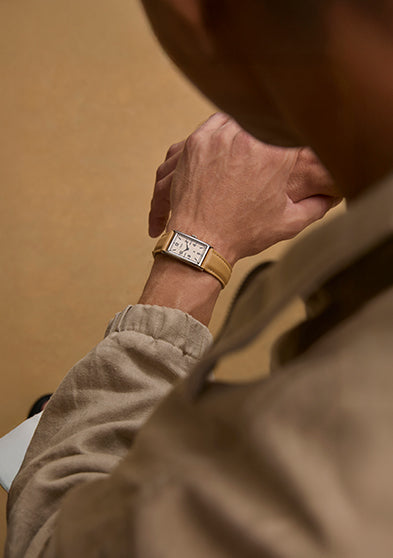 Top-down view of the Timex x Todd Snyder 1976 Lexington watch with a cream dial and tan leather strap worn on a wrist with a neutral outfit.