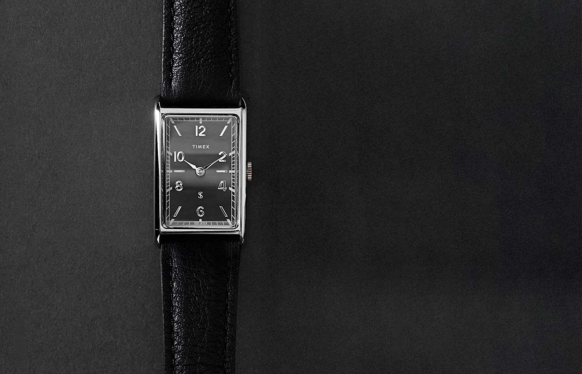 Timex x Todd Snyder 1976 Lexington rectangular watch with a black dial and black leather strap displayed vertically on a dark background