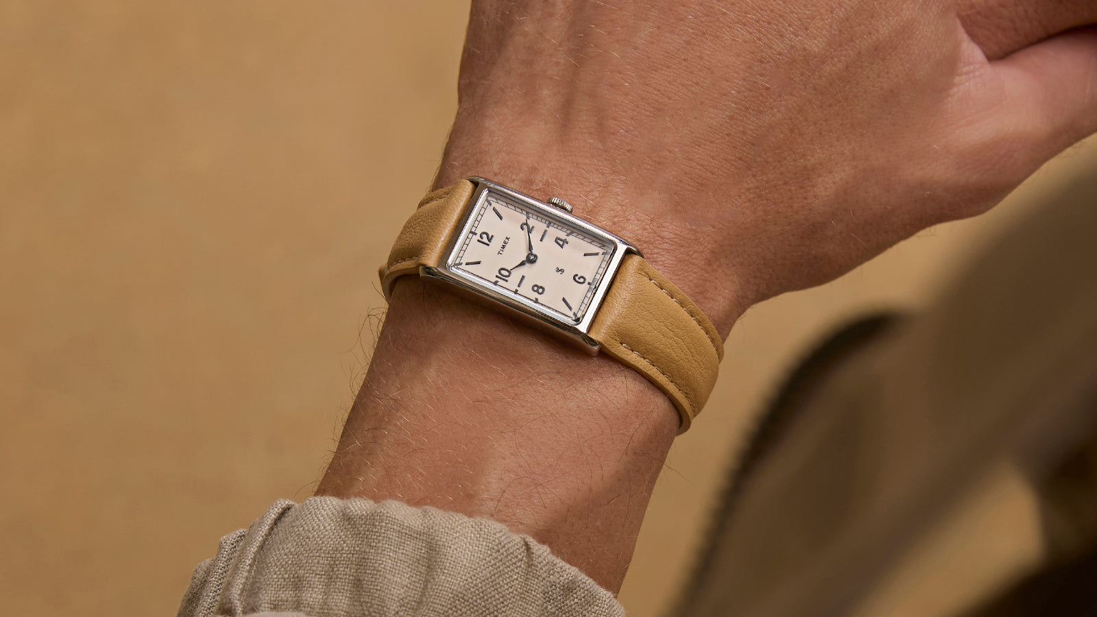 Close-up of the Timex x Todd Snyder 1976 Lexington watch with a cream dial and tan leather strap on a wrist.