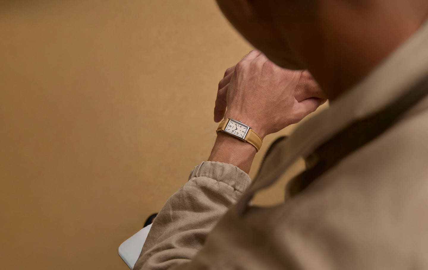 Overhead view of a person wearing a Todd Snyder x Timex 1976 Lexington watch with a rectangular dial and tan leather strap, paired with neutral-toned clothing.