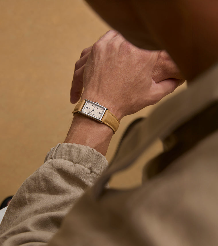 Overhead view of a person wearing a Todd Snyder x Timex 1976 Lexington watch with a rectangular dial and tan leather strap, paired with neutral-toned clothing.