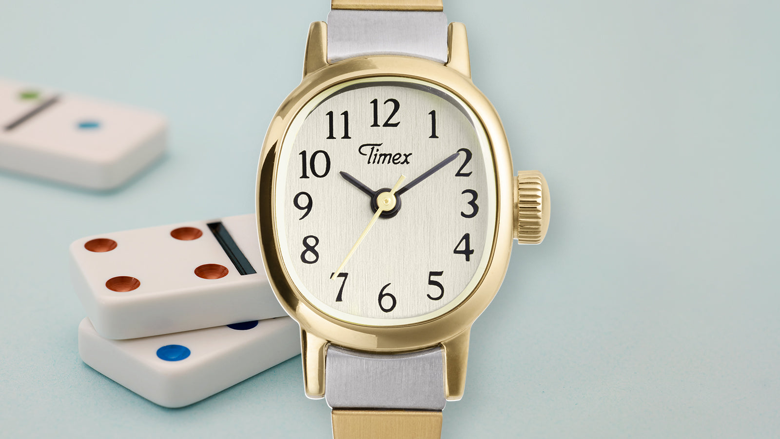 Close-up of Cavatina® Mini watch showing gold-tone oval case, cream dial, black Arabic numerals, and two-tone stainless steel bracelet.