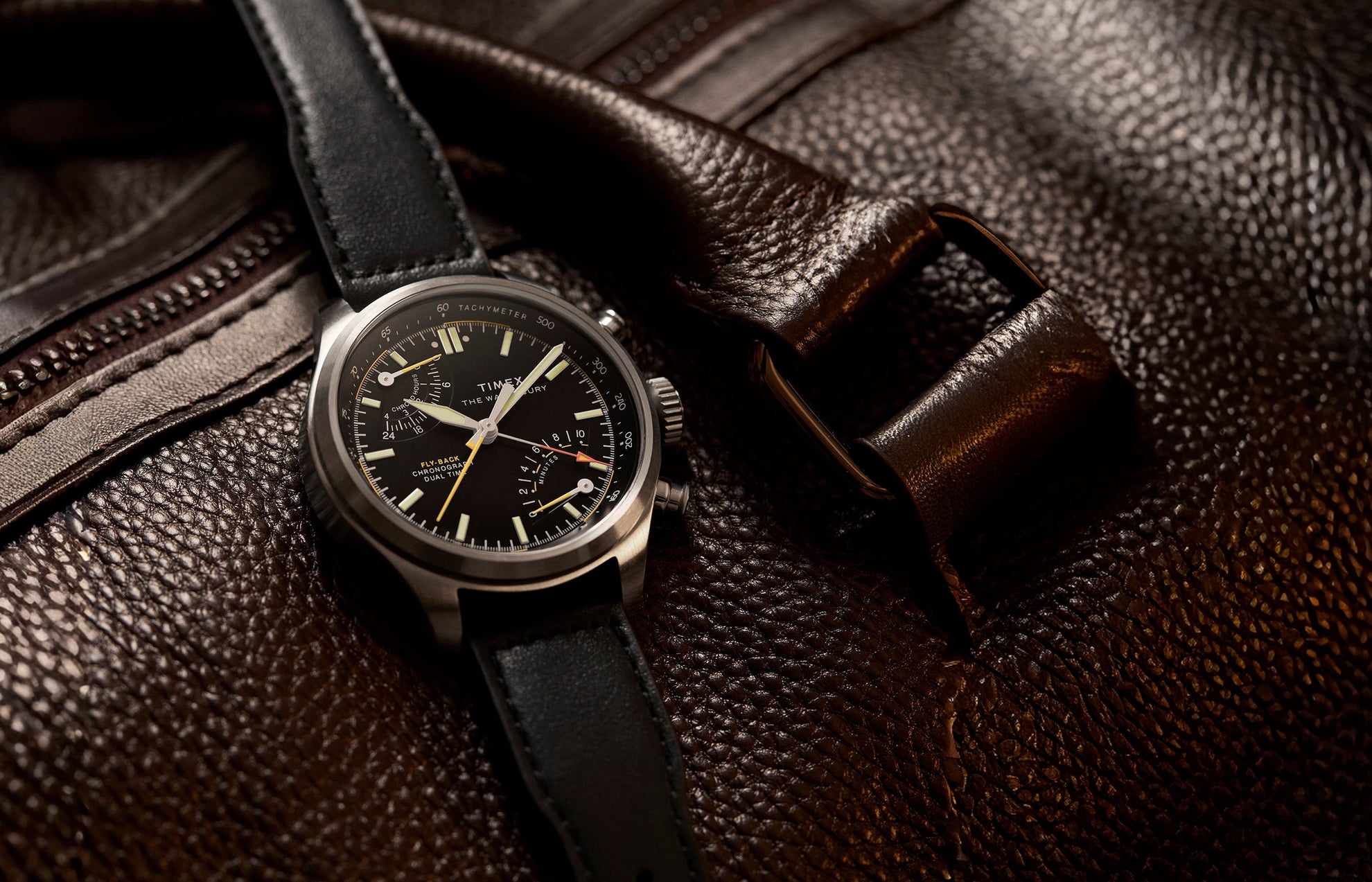 Timex Waterbury Ace Fly-Back Chronograph watch with black dial and leather strap resting on textured brown leather bag