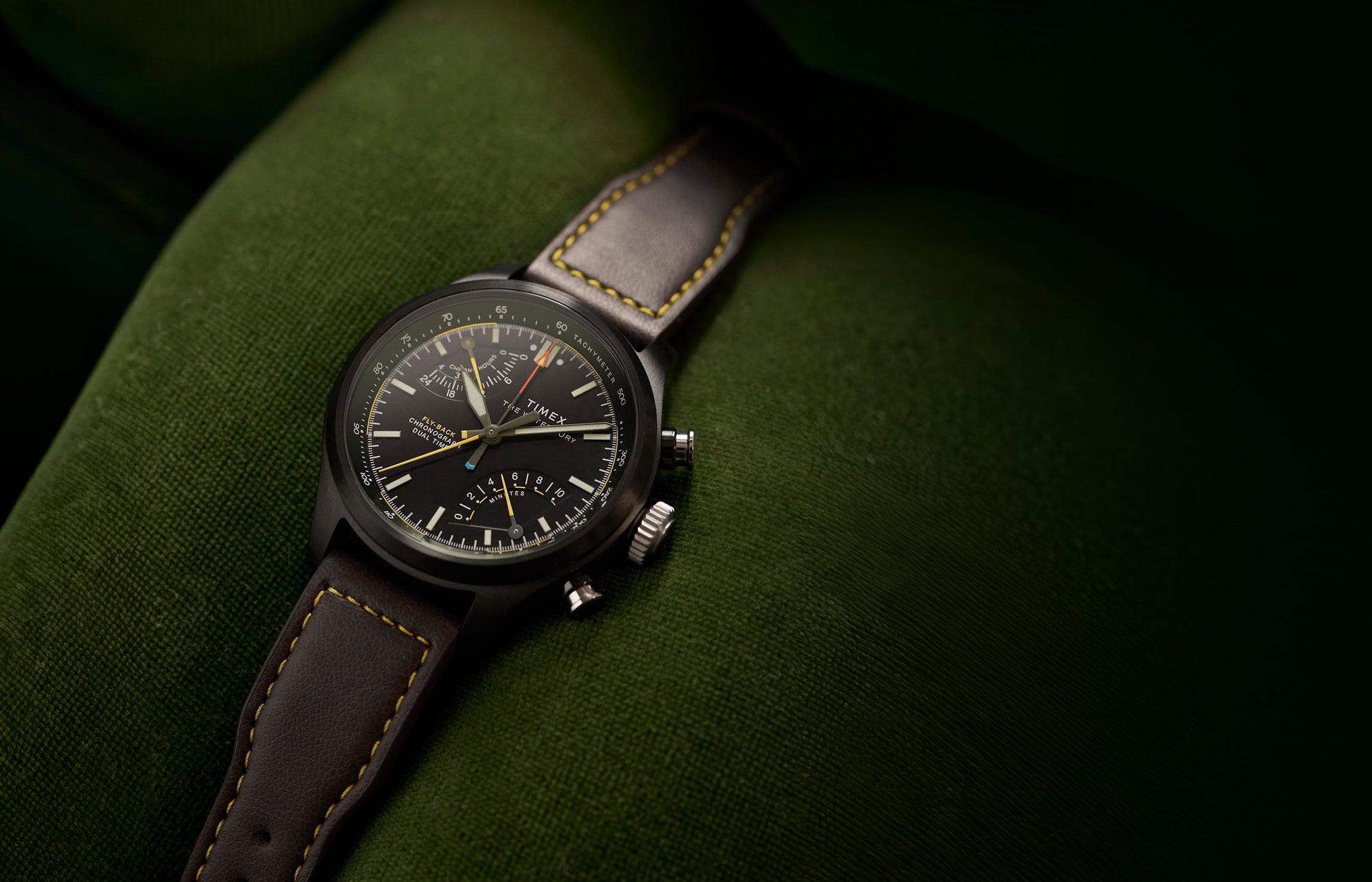 Timex Waterbury Ace Fly-Back Chronograph with black dial and brown leather strap on green fabric surface