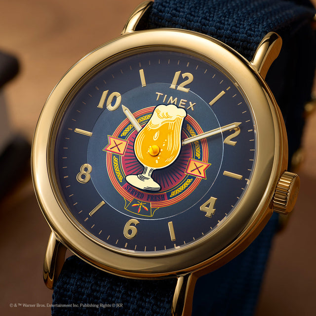 Harry Potter x Timex Weekender Butterbeer watch with navy dial, gold-tone case, and Butterbeer graphic at center.