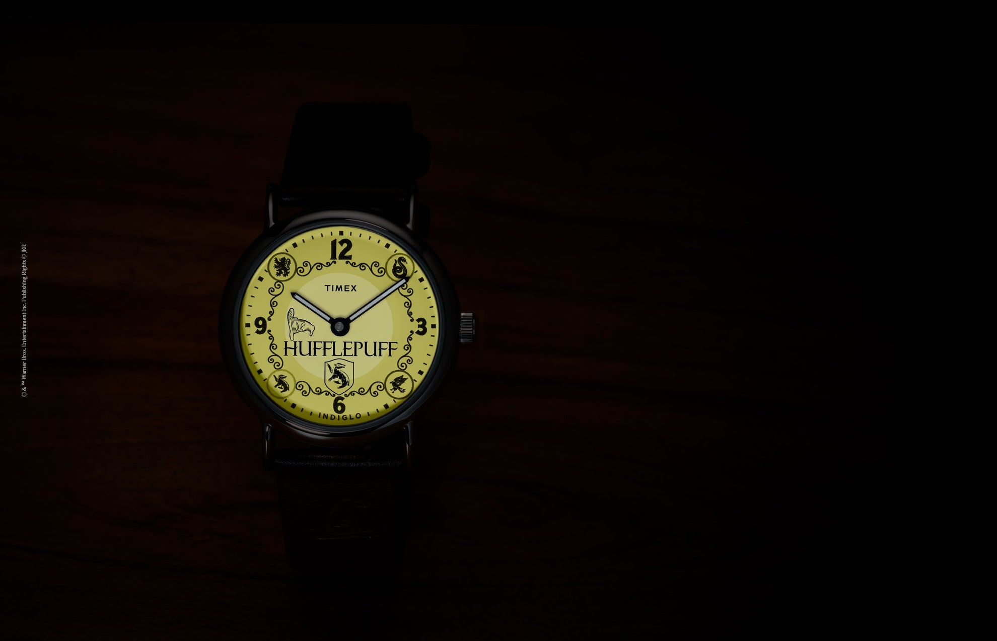 Harry Potter x Timex Weekender Hufflepuff watch illuminated in yellow INDIGLO mode showing Hufflepuff name and house crest.