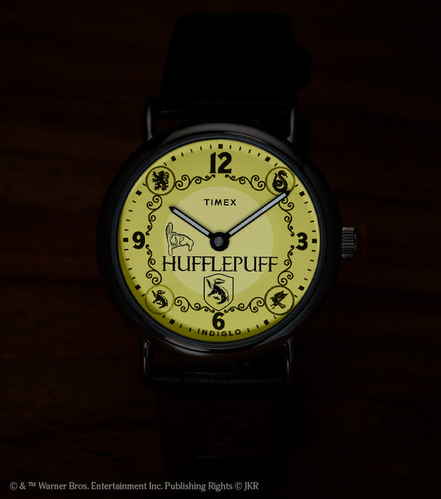 Harry Potter x Timex Weekender Hufflepuff watch illuminated in yellow INDIGLO mode showing Hufflepuff name and house crest.