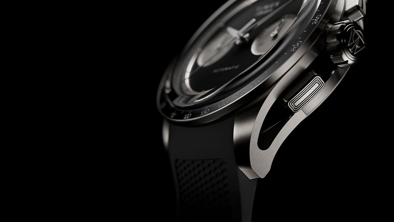 Macro view of the Timex Atelier Chronograph Automatic M1a Ti showcasing the brushed titanium case, chronograph pusher, tachymeter bezel, and integrated black rubber strap.