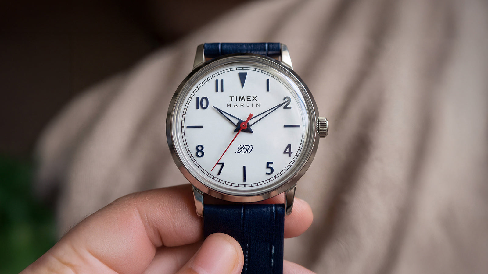 Marlin America 250 watch held in hand, showcasing the white dial, blue numerals, red seconds hand, and blue leather strap.