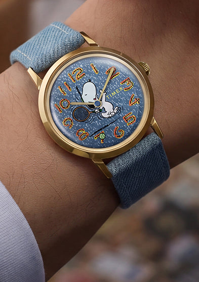 Lifestyle image of the Peanuts® x Timex Marlin® 1965 Reissue Inspired Snoopy Tennis watch worn on the wrist during a casual indoor setting.