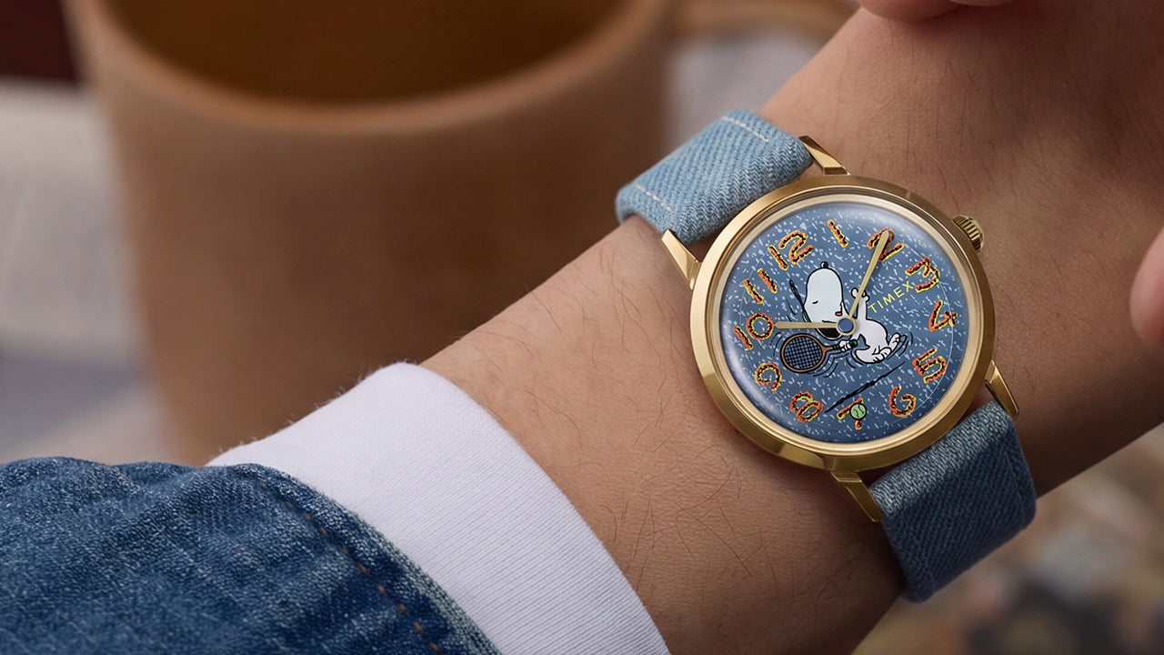 Lifestyle image of the Peanuts® x Timex Marlin® 1965 Reissue Inspired Snoopy Tennis watch worn on the wrist during a casual indoor setting.