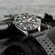 Timex Deepwater Meridian 300 Titanium HEV Automatic dive watch resting on scuba diving gear near the ocean shoreline.