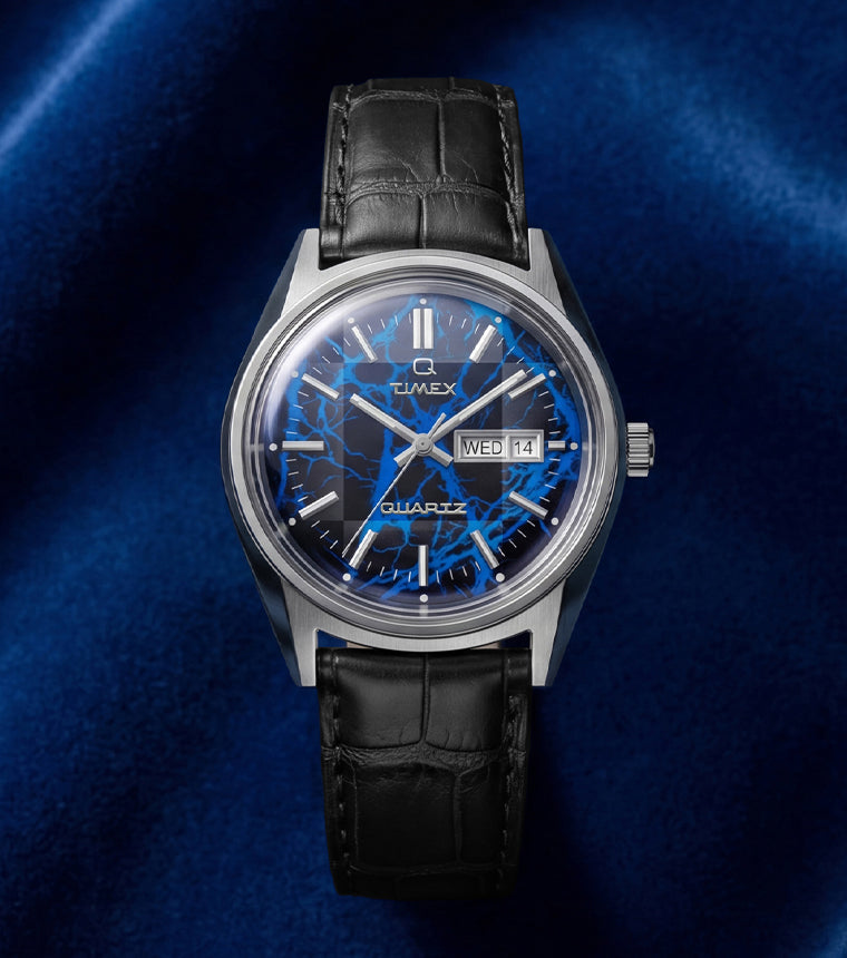 Q Timex Blue Vega watch with electric blue lightning-pattern dial on black leather strap against deep blue satin background