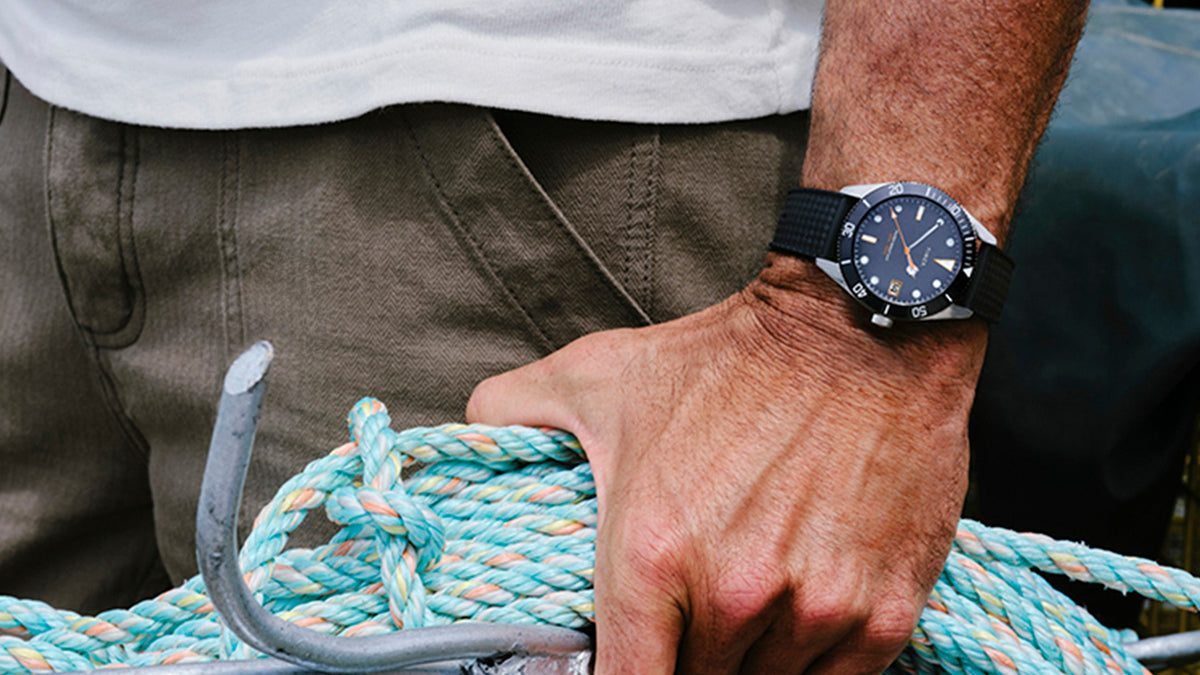 Man wearing the Bespoke Post x Timex Heritage 66 watch with a black strap while holding coiled rope.