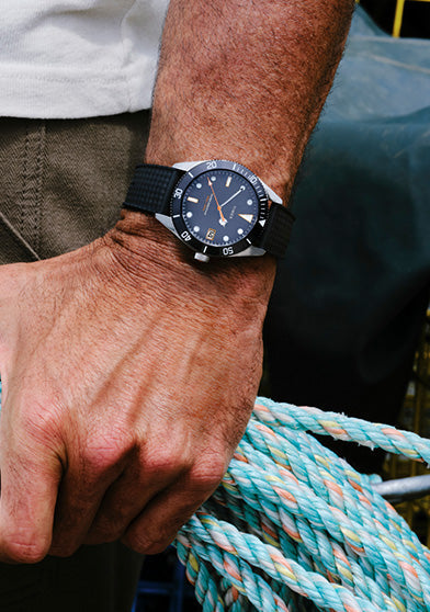 Man wearing the Bespoke Post x Timex Heritage 66 watch with a black strap while holding coiled rope.
