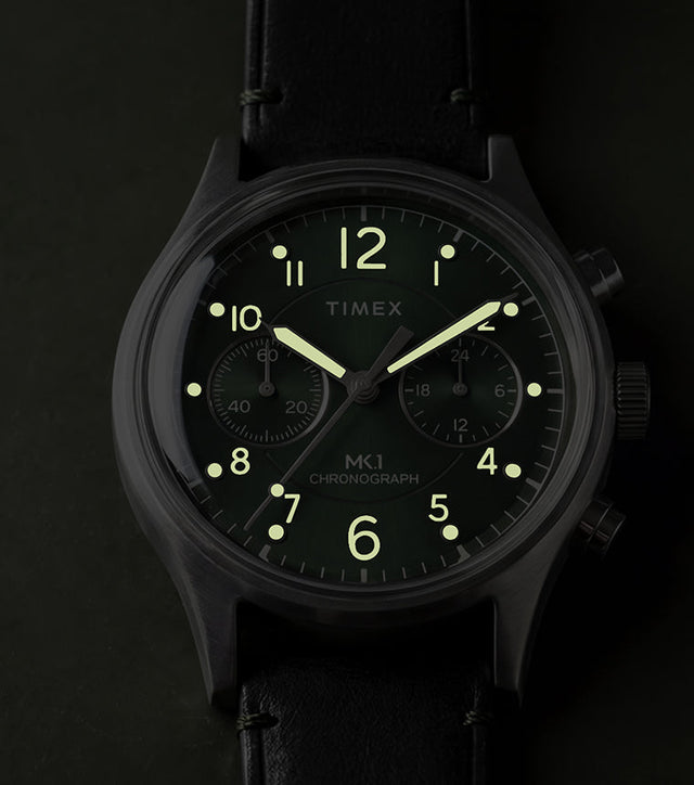 Timex MK1® Chronograph watch showing glowing luminous hands and hour markers on a green dial in low light.