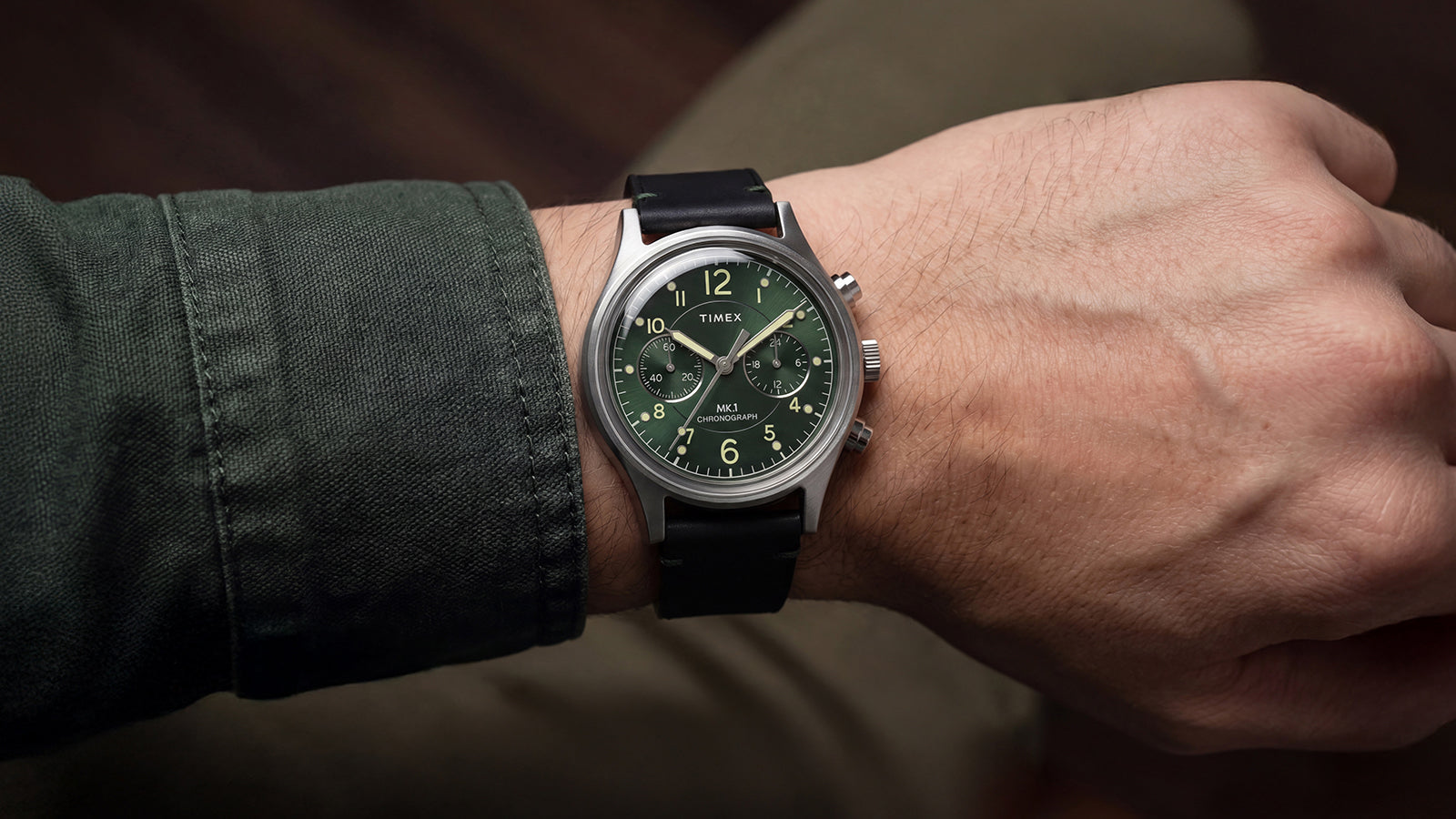 Person wearing the Timex MK1® Chronograph with a green dial, black leather strap, and brushed stainless steel case.