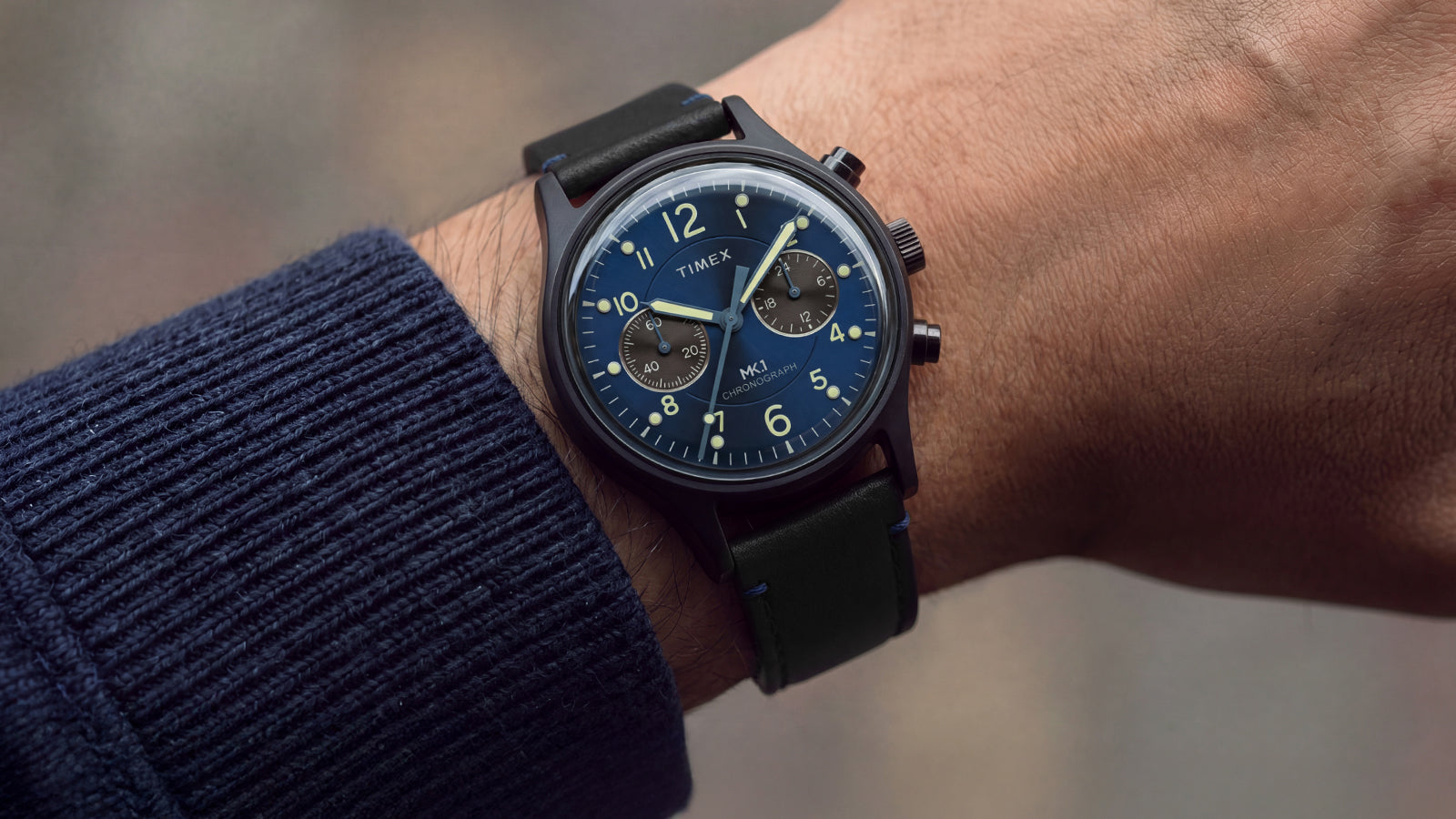 Person wearing the Timex MK1® Chronograph with a blue dial, black leather strap, and black case.