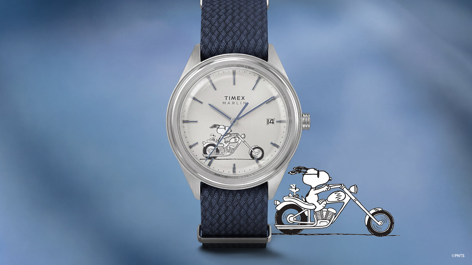 Front view of the Peanuts® x Timex Marlin® Jet Automatic Easy Rider watch showcasing a white dial with Snoopy riding a motorcycle artwork, blue hour markers, date window, silver-tone case, and blue woven strap against a blue gradient background.