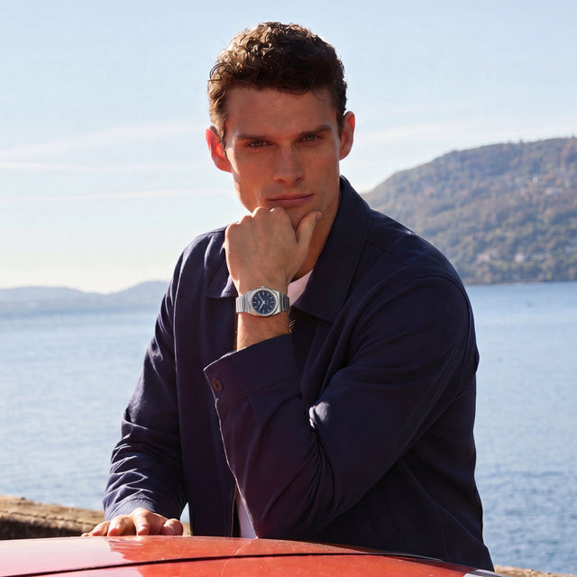 Person wearing the Timex Q Marbella stainless steel watch with a blue dial while seated outdoors by the waterfront.