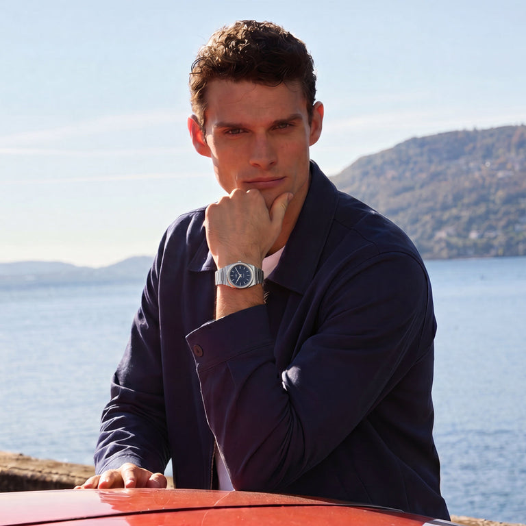 Person wearing the Timex Q Marbella stainless steel watch with a blue dial while seated outdoors by the waterfront.