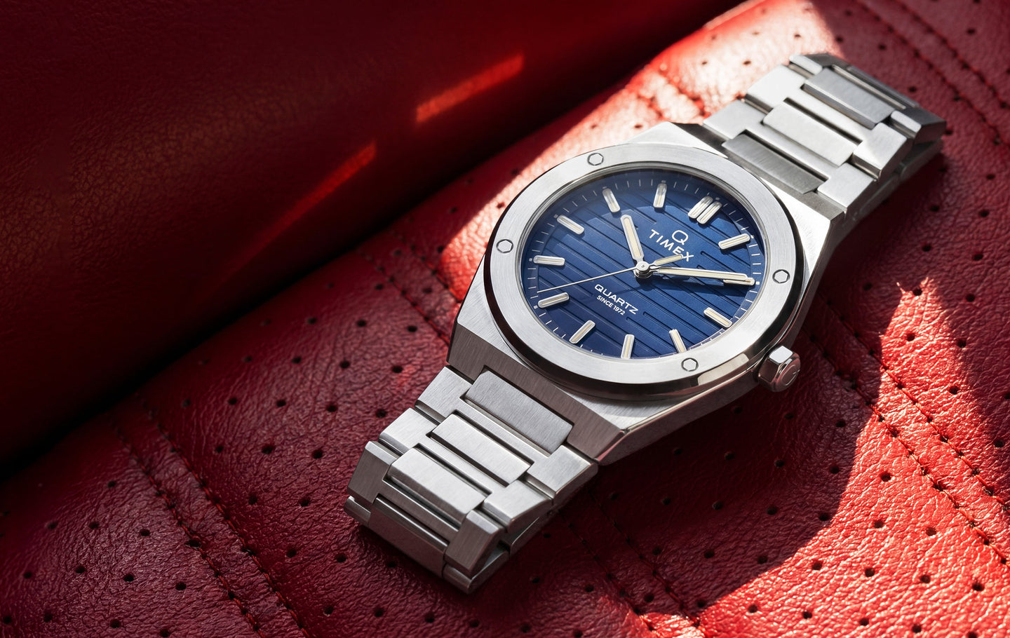 Q Timex Marbella stainless steel watch with a blue dial resting on a red leather seat.