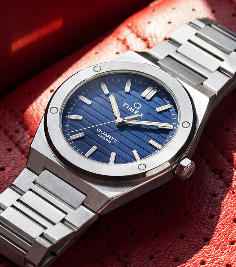 Q Timex Marbella stainless steel watch with a blue dial resting on a red leather seat.