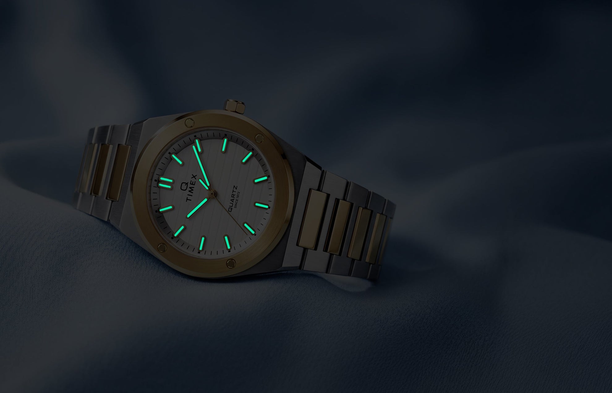 Q Timex Marbella two-tone stainless steel watch with glowing Indiglo® hands and hour markers in low light.