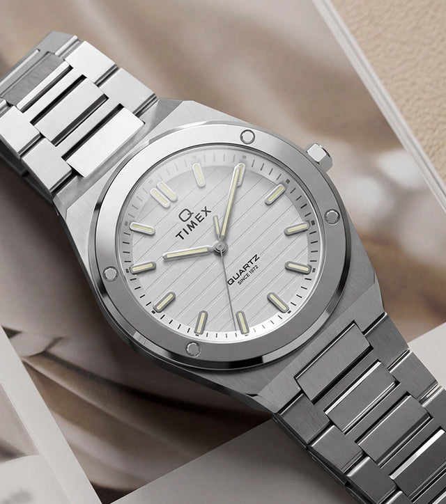 Q Timex Marbella stainless steel watch with a silver dial and integrated bracelet displayed on an open magazine.
