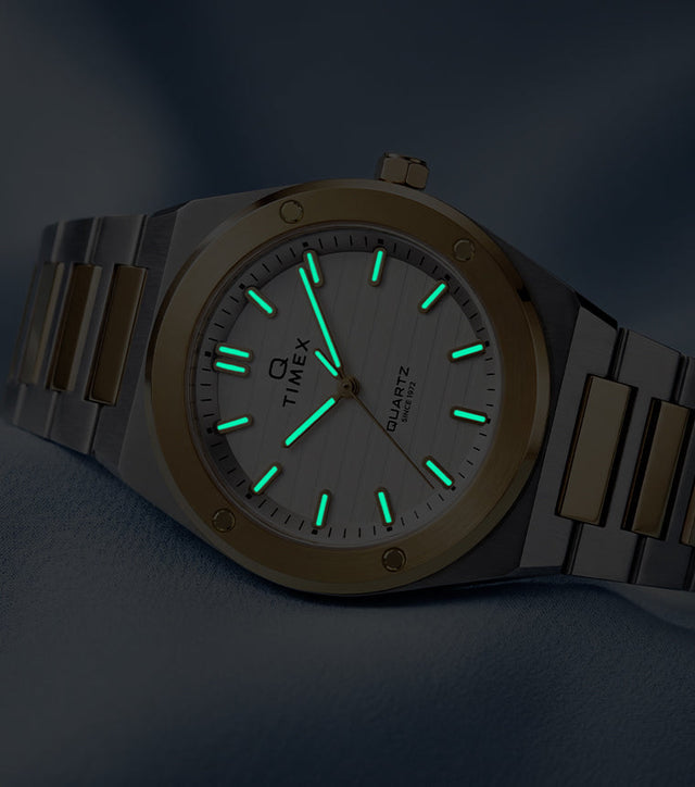 Q Timex Marbella two-tone stainless steel watch with glowing Indiglo® hands and hour markers in low light.